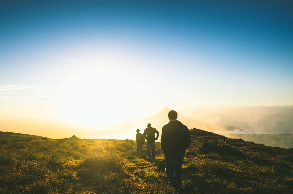 Drei Wanderer gehen eine Wanderweg entlang, dem Sonnenuntergang entgegen.