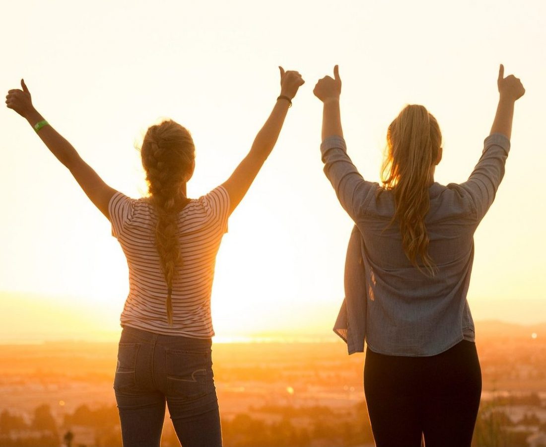 Zwei Frauen im Sonnenuntergang - ©StockSnap/Pixabay Zwei Frauen stehen mit hochgereckten Daumen auf einem Aussichtspunkt und schauen in den Sonnenuntergang.
